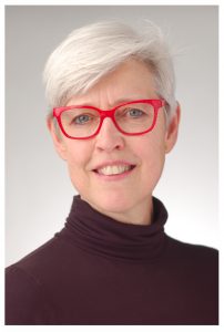 A woman with short white hair and red glasses. She is smiling.