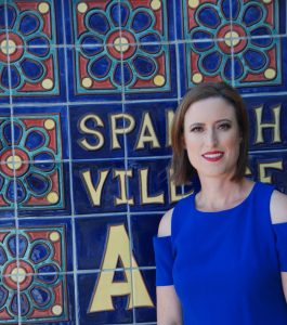 Erin Hogan is standing in front of street sign in Spain that consists of brightly colored ceramic tiles.