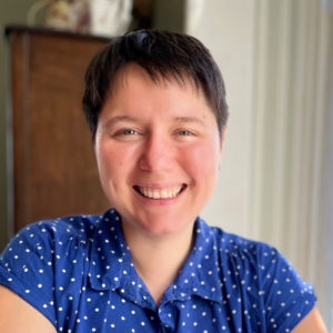 Lindsay Johnson, a white woman with short brown hair, is smiling at the camera. She is wearing a blue shirt with white polka dots.