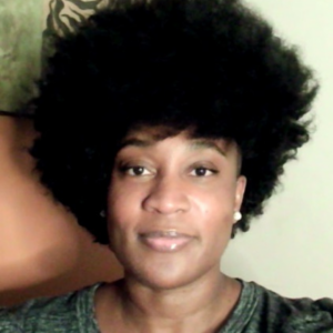 A Black woman with big hair is looking, unsmiling, at the camera.